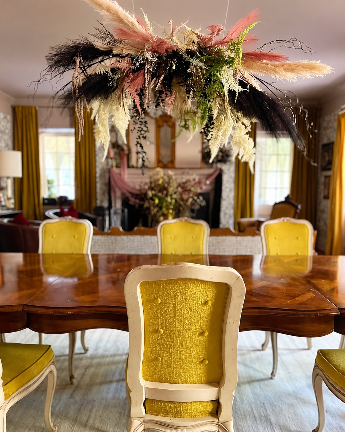 Dining room with yellow chairs beneath a hanging dried-botanical installation