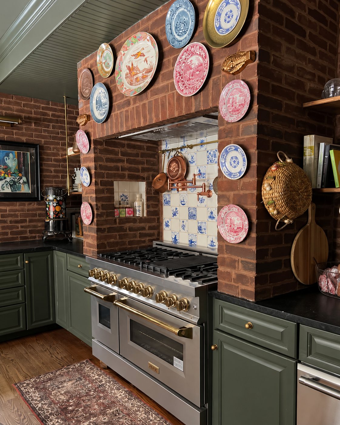 Green-cabinet kitchen with a brick range hood hung with antique decorative plates