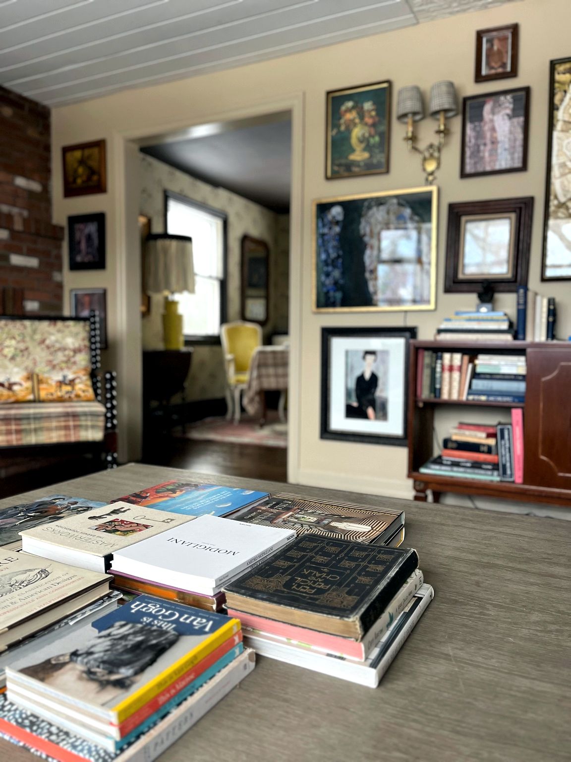 Living room with a salon-style gallery wall, stacked art books and an antique bookcase
